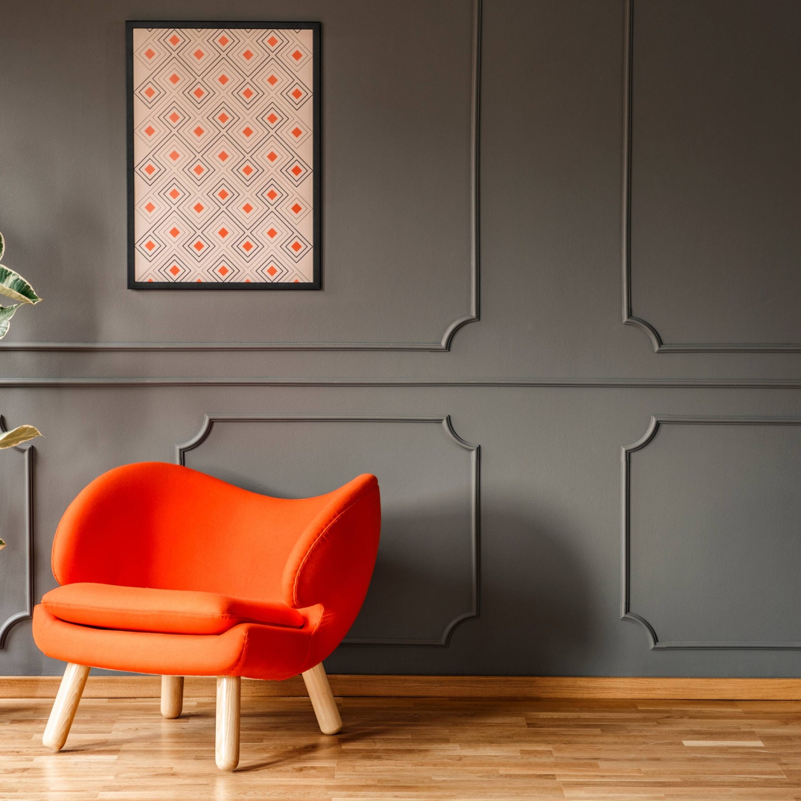 dark earth colored wainscoting with a bright orange chair in front of it as well as artwork